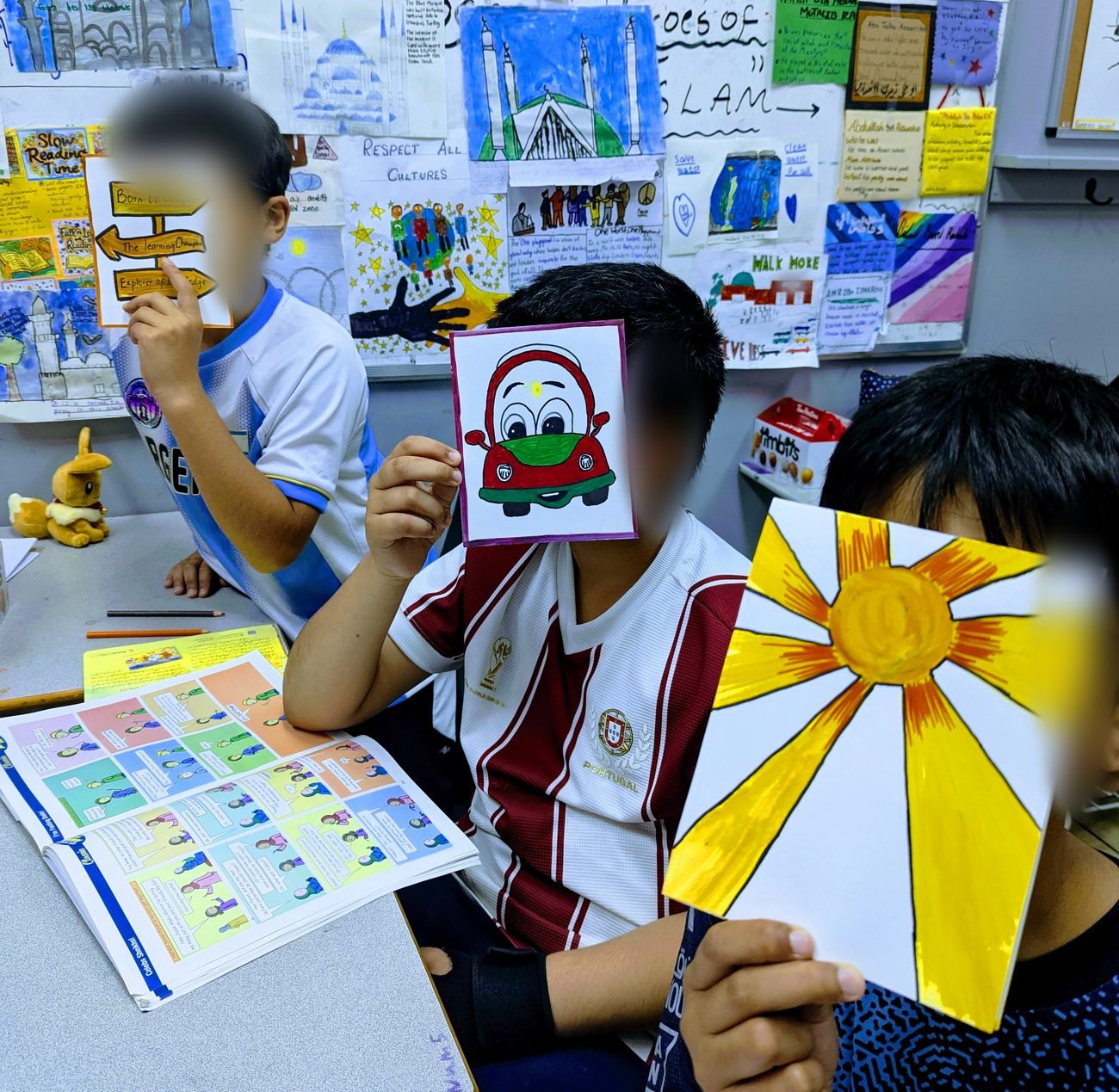 Students at their desks holding up their drawings during show and tell