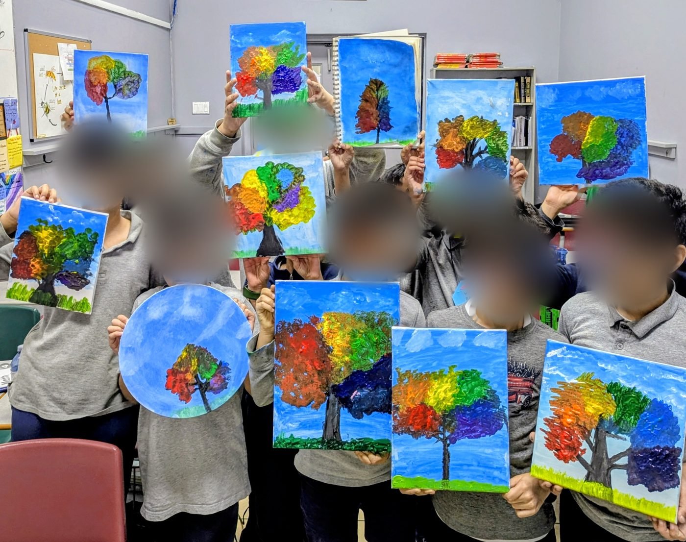 A class of students holding up their acrylic paintings of a rainbow-leaved tree